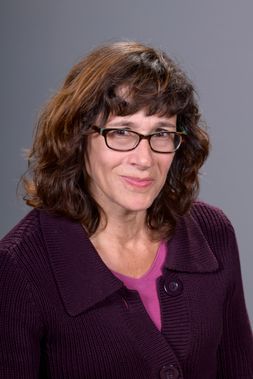 Karen Weiss smiles for a professional headshot. She has dark brown hair, brown eyes, and is wearing brown-framed glasses.