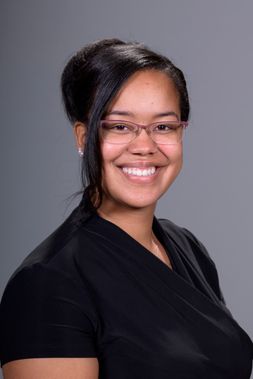 Stephanie M. House-Niamke smiles for a professional headshot. She is a Black woman with dark brown hair, and she is wearing pink wire-frame glasses.